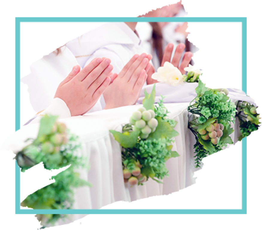 Bride praying with hands clasped, surrounded by white flowers and green grapes in a bright wedding setting