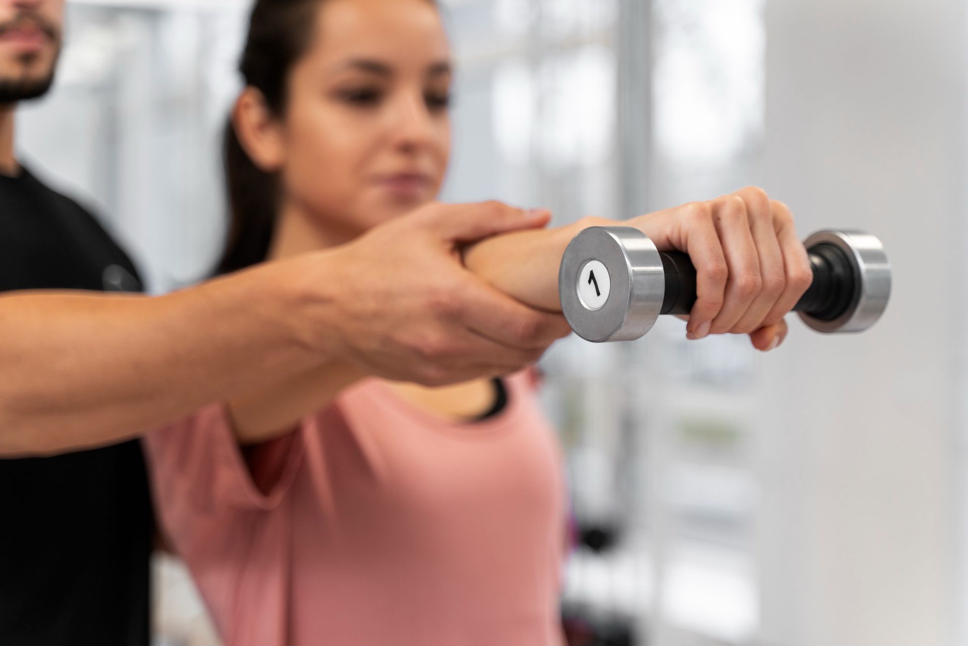 A man is helping a woman lift a dumbbell in a gym.