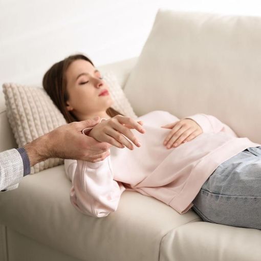 A woman is laying on a couch with her eyes closed while a man holds her arm.