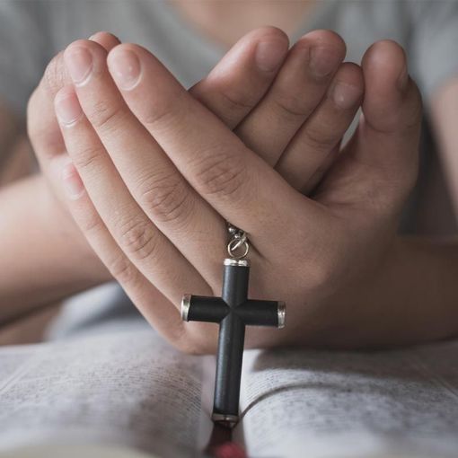 A person is praying with a cross in their hands