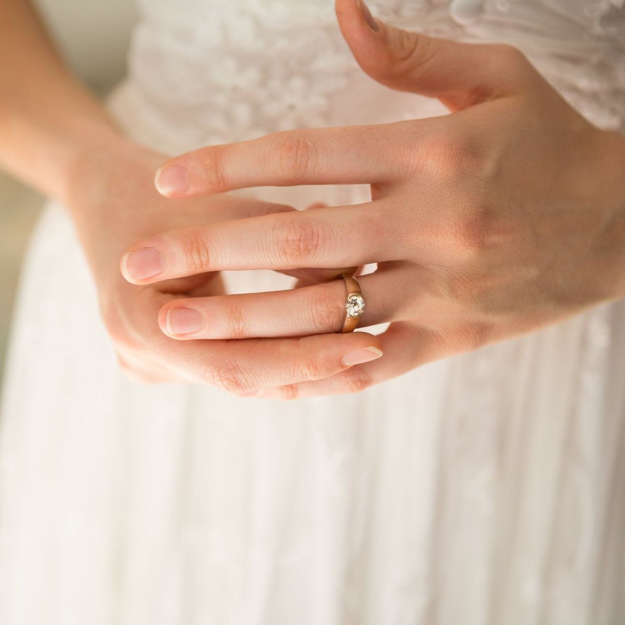 A woman in a white dress is wearing a wedding ring on her finger.