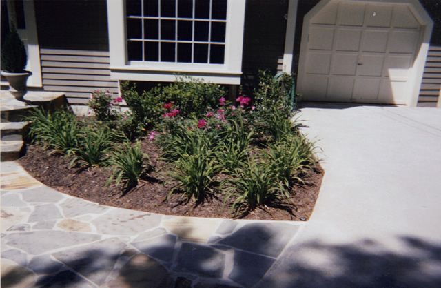 A driveway with flowers and bushes in front of a house