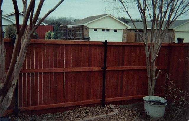 A red wooden fence is surrounded by trees and houses.