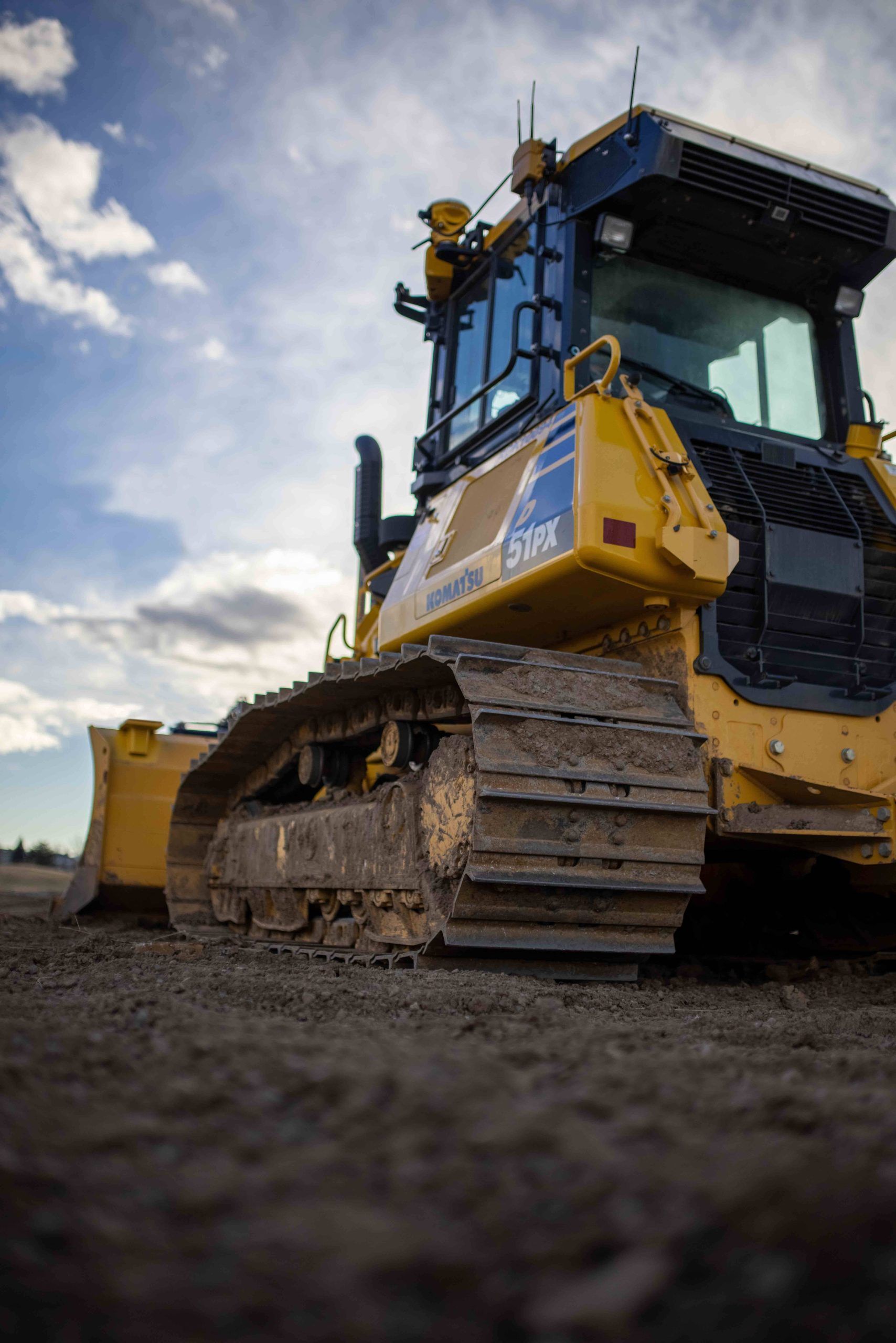 Yellow bulldozer on a dirt road under a cloudy sky, viewed from a low angle