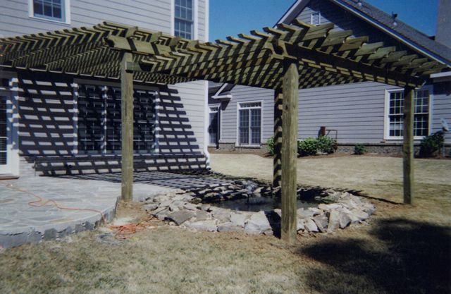 A wooden pergola is in the backyard of a house