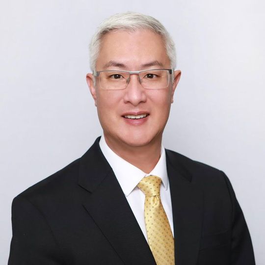 Man in suit and glasses smiling at the camera. Yellow tie and white collared shirt.
