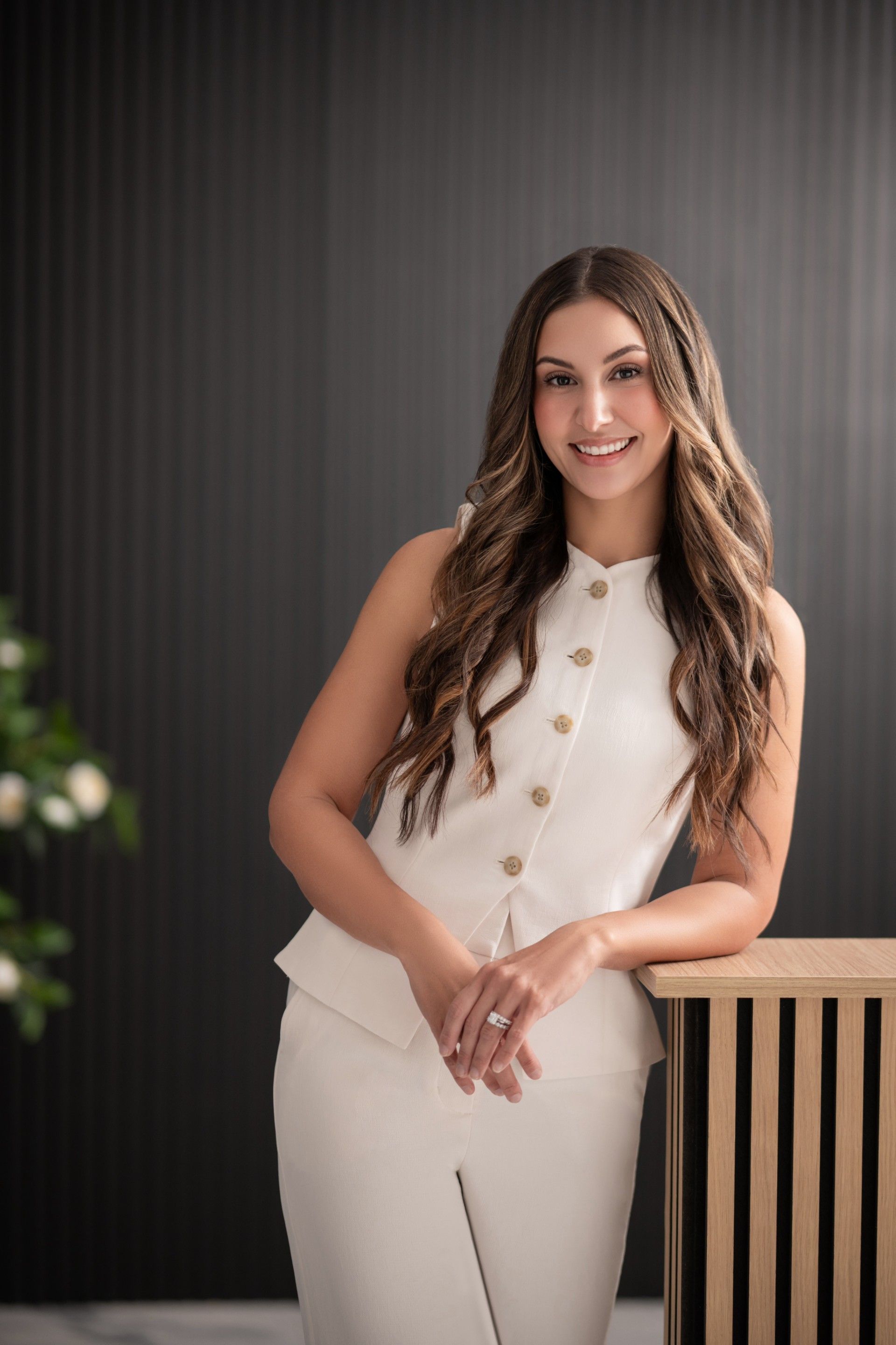 Woman in white outfit leaning on a wooden counter, smiling.