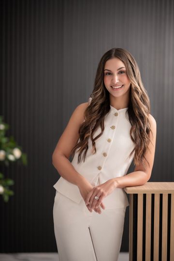 Woman in white outfit leaning on a wooden counter, smiling.