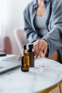 Person applying skincare drops beside a laptop on a white table