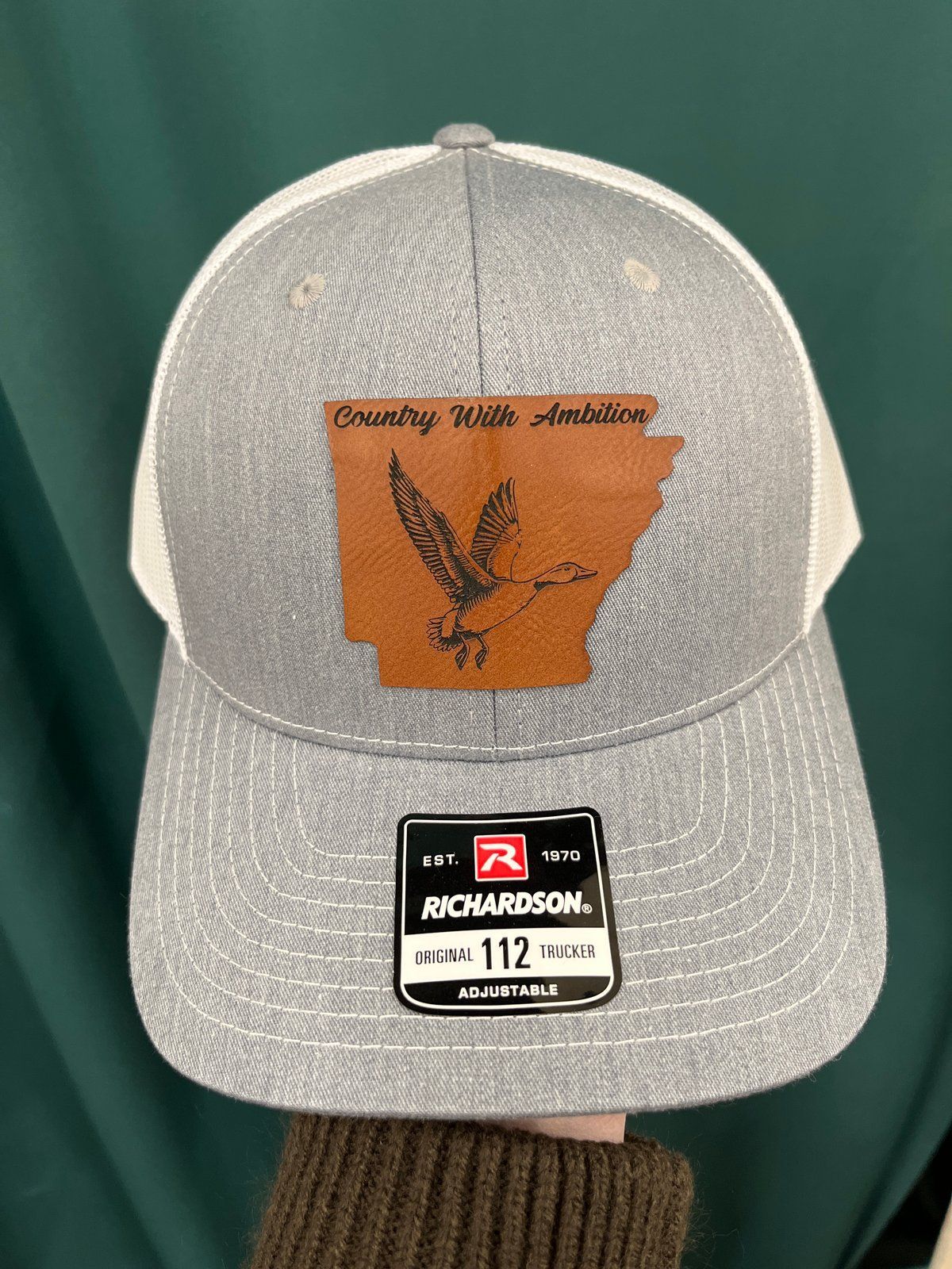 Gray and white Richardson trucker hat with a leather duck patch
