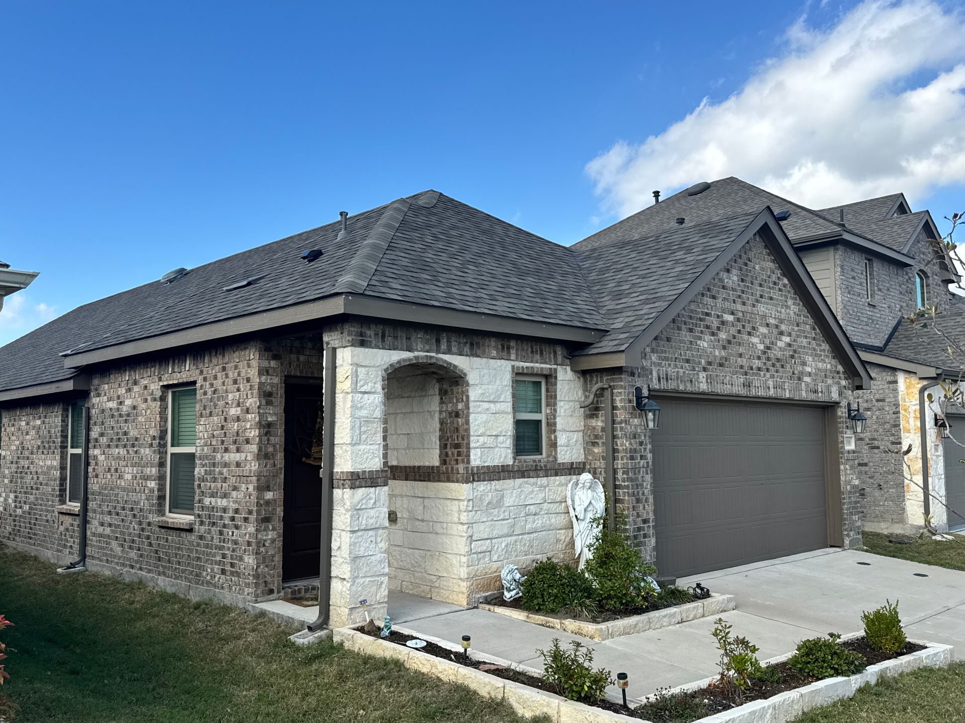 Brick house exterior with dark roof, attached garage, and small front walkway under a blue sky