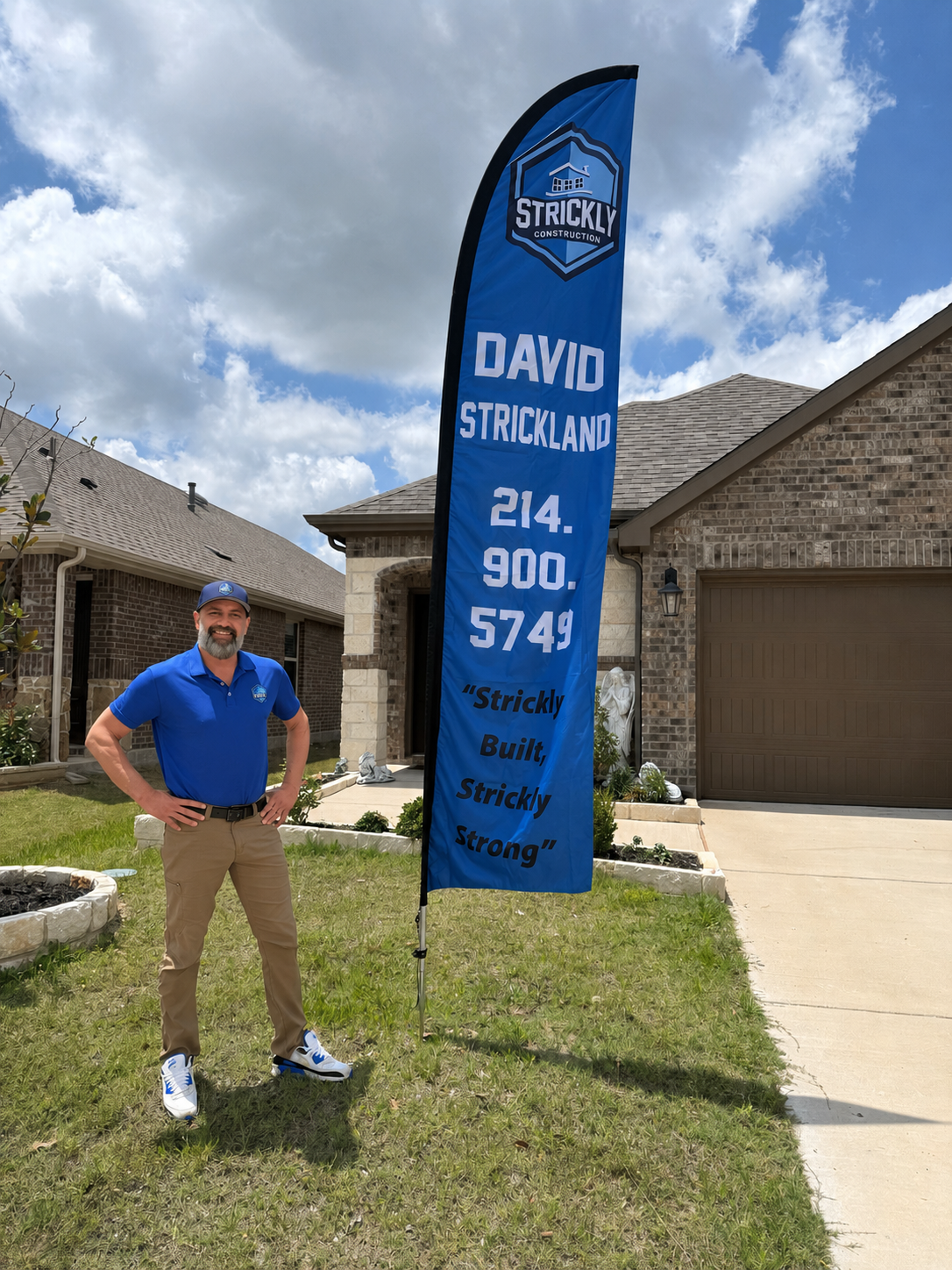 Man standing beside a blue “David Strickland” real estate flag in front of a house, waving.