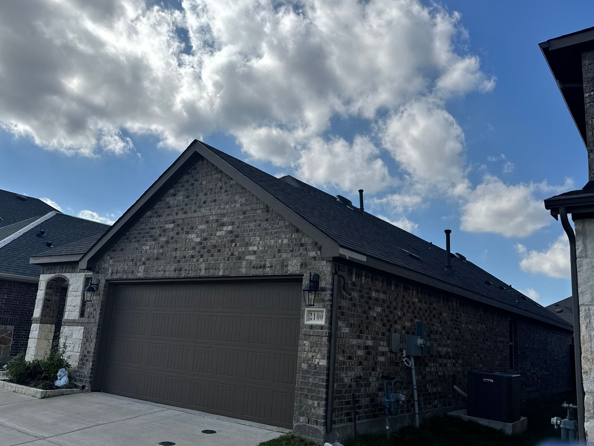 Brick suburban house with dark garage door under a cloudy blue sky