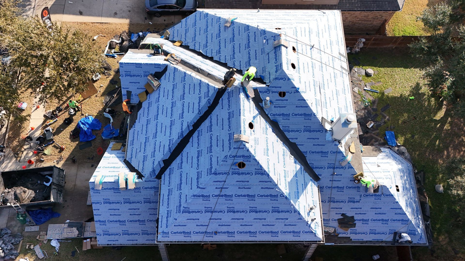 Aerial view of a house roof under construction with workers and roofers laying shingles