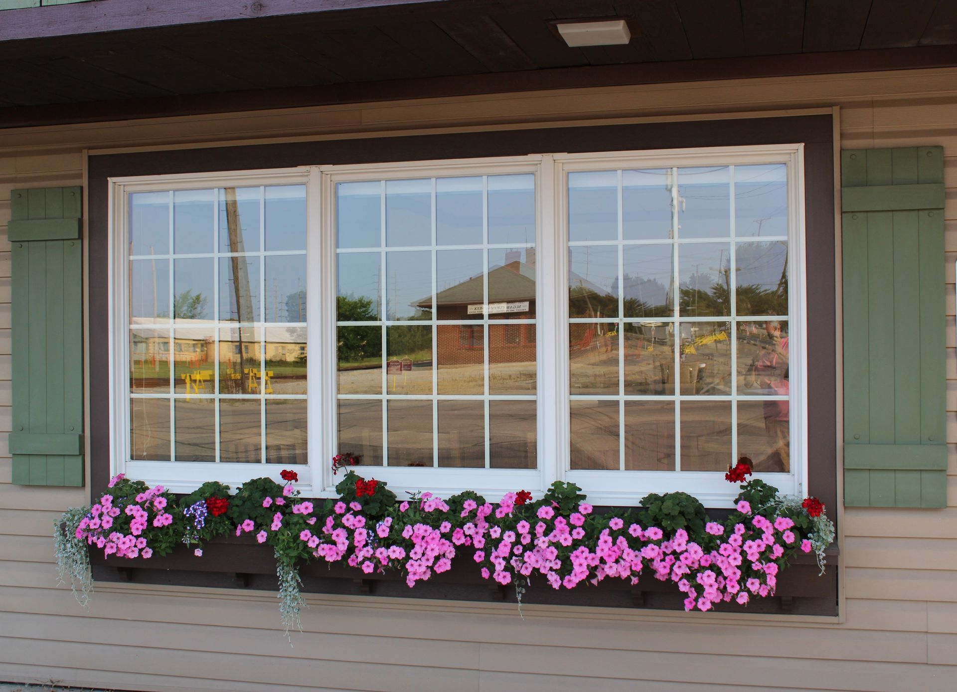 Window box of pink flowers beneath a large white-framed window on a house porch