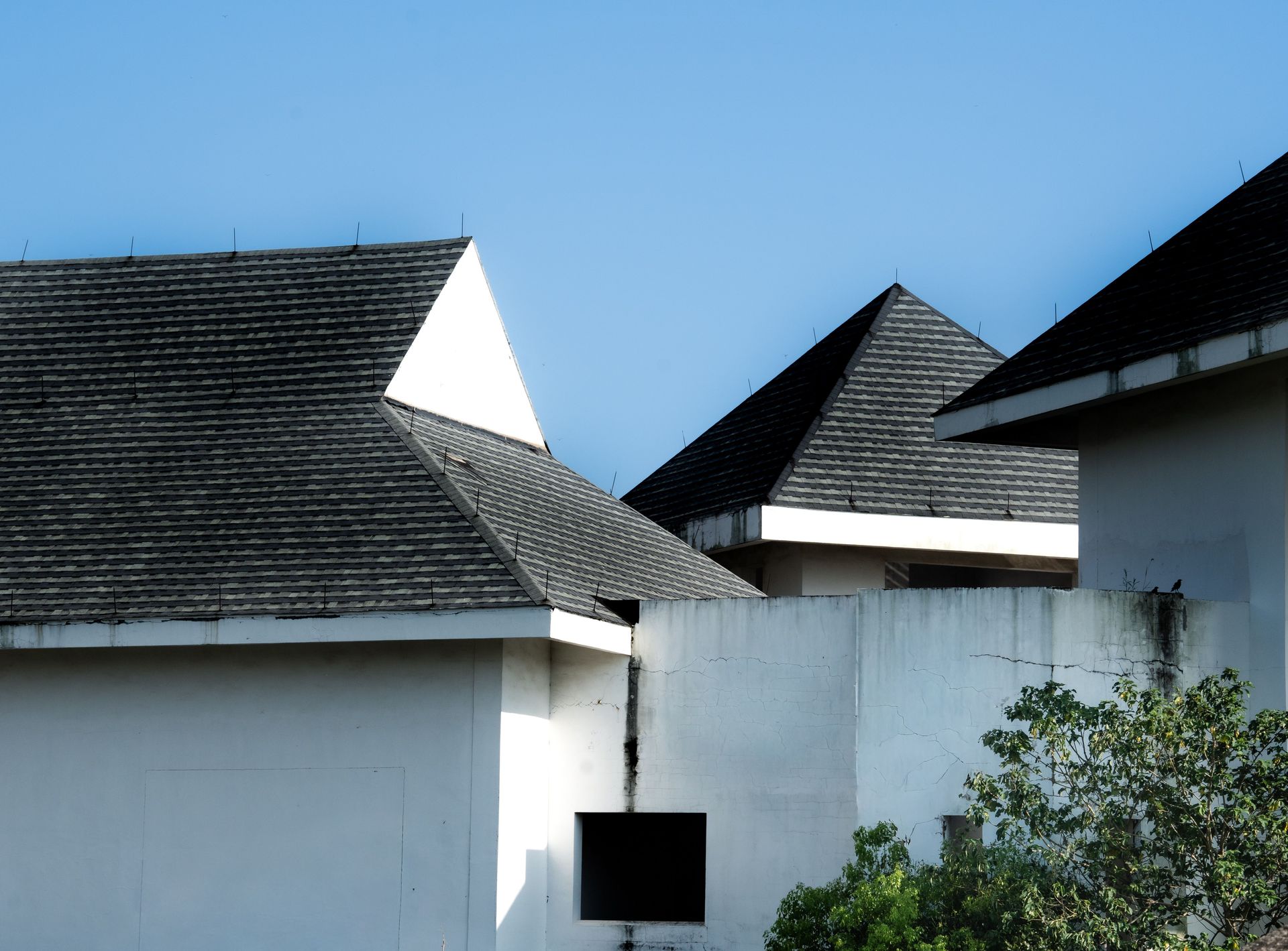 White buildings with dark shingled roofs against a clear blue sky, partly framed by greenery
