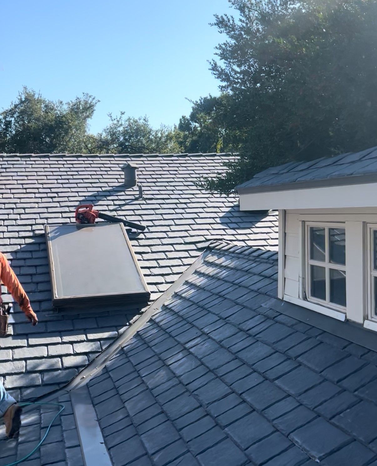Roofer working on gray shingle roof beside skylight and white dormer window