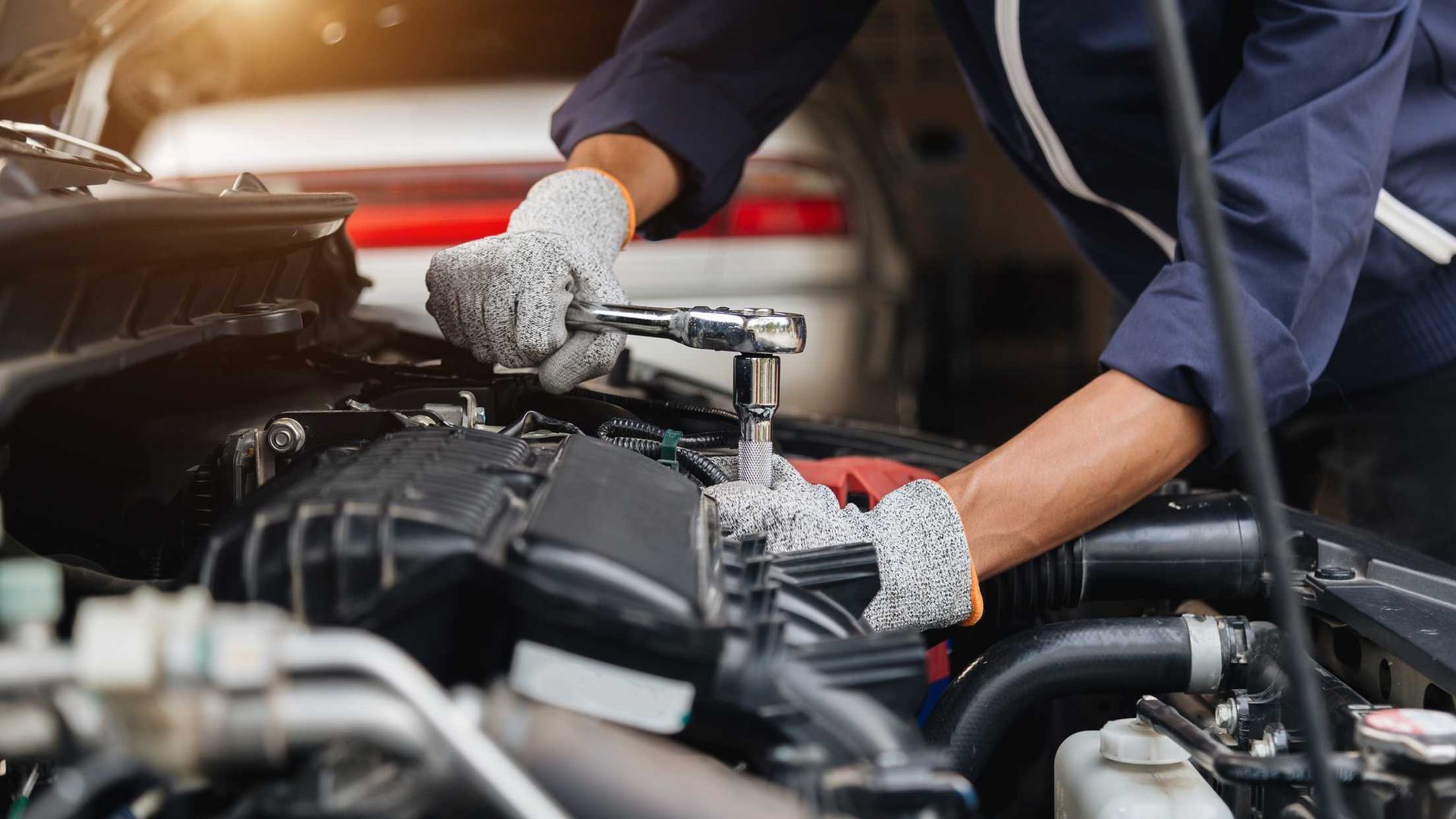 Mechanic working on a car engine in a garage, wearing gloves and handling tools