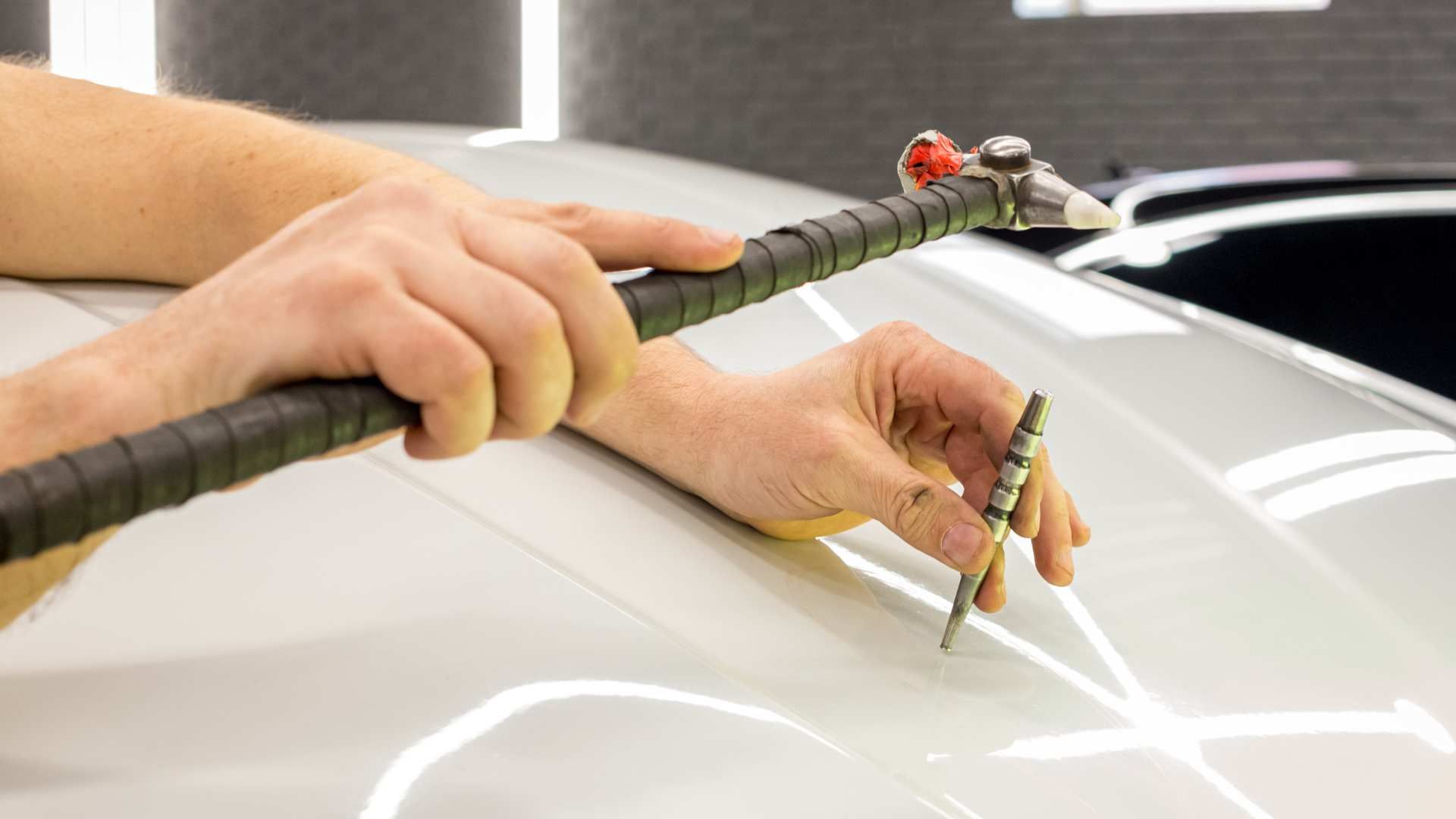 Hands guiding a car body repair tool over a white vehicle in a workshop