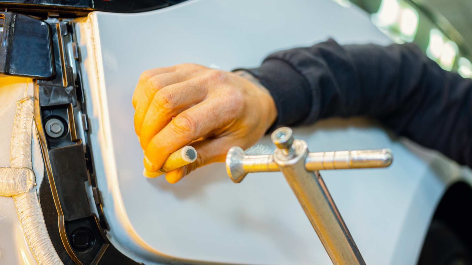 Hand using a polishing tool on a white car door near the hinge