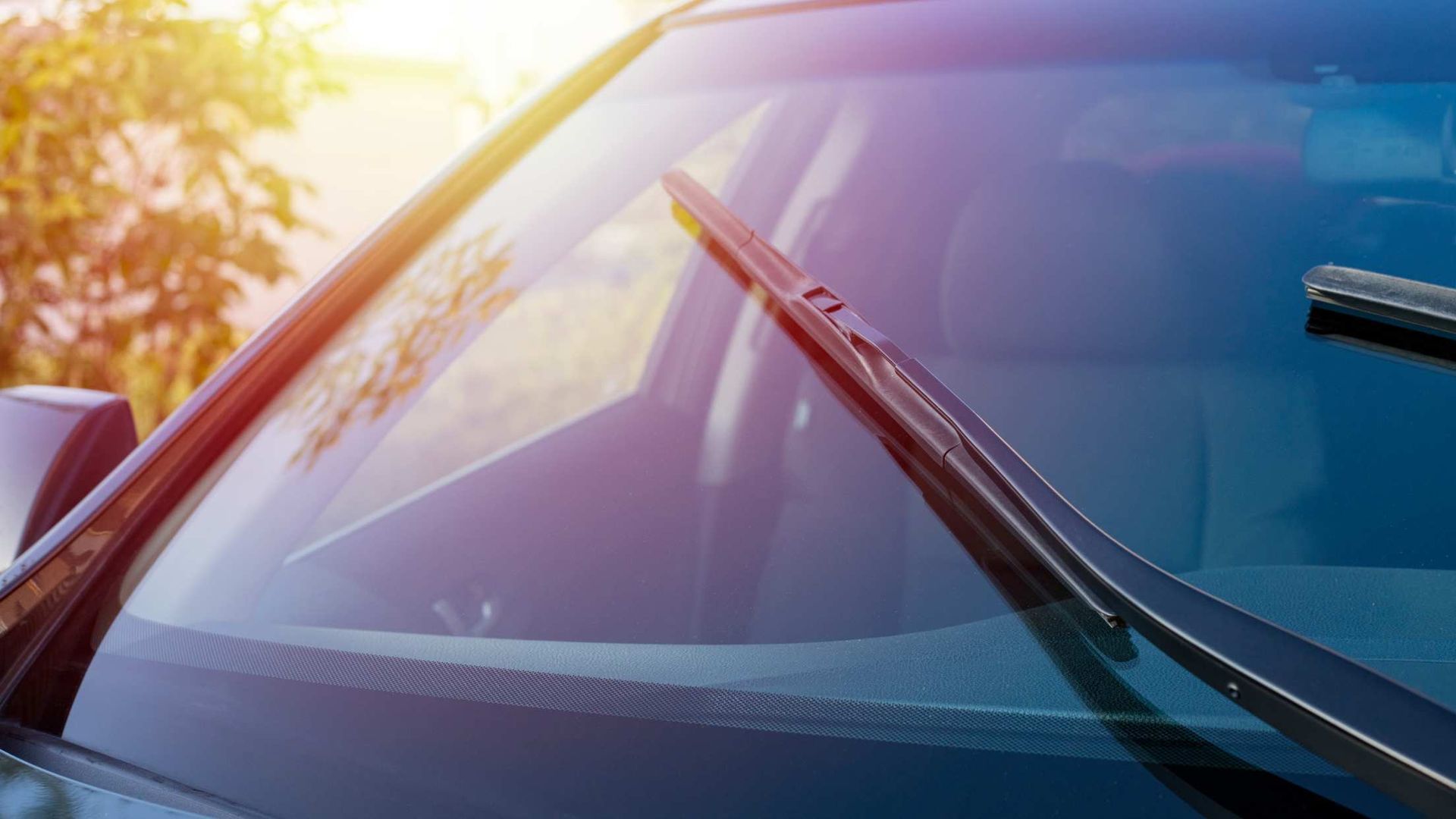 Close-up of a car windshield with a wiper and warm sunlight glare