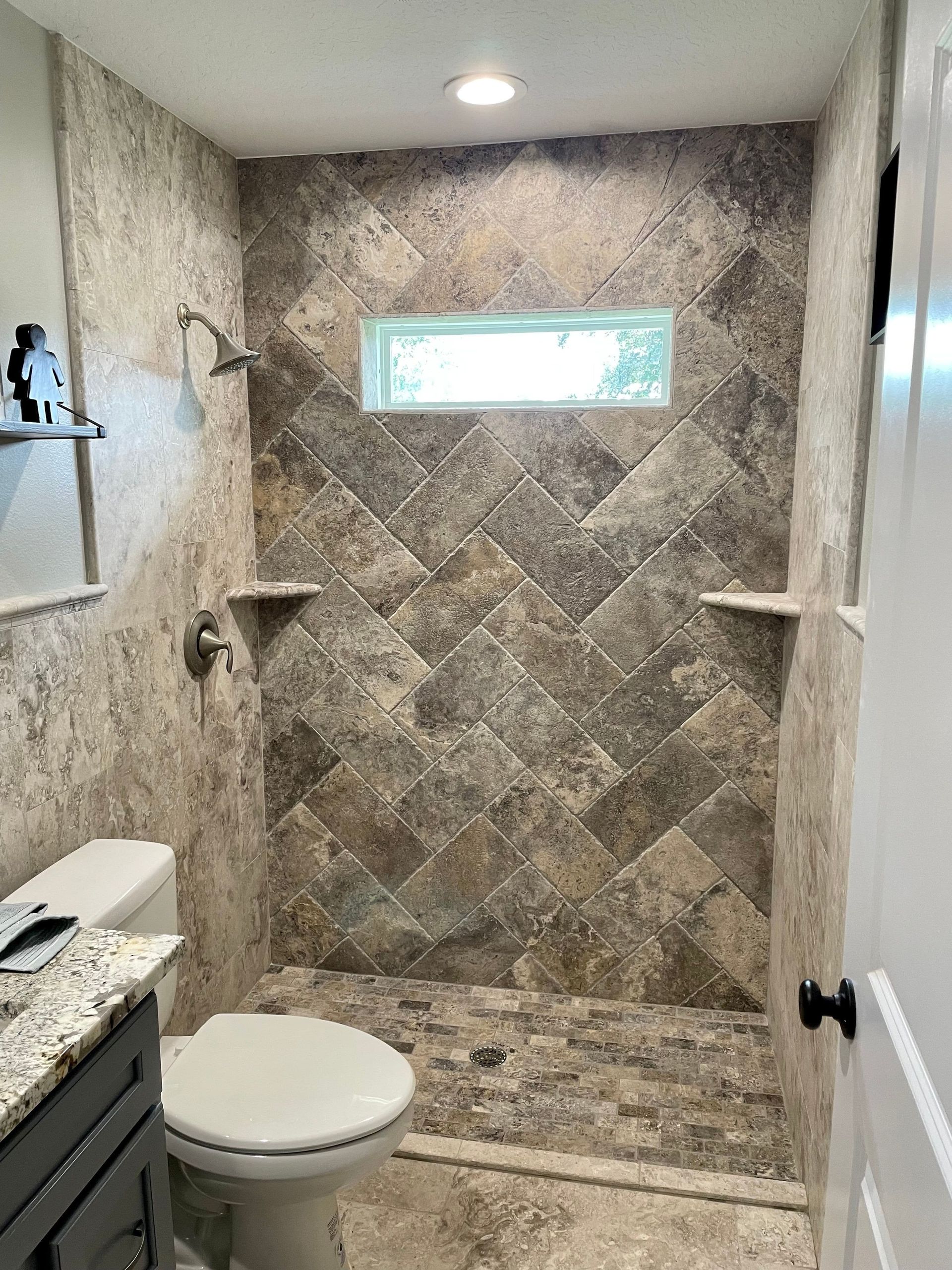 Small bathroom with a tiled walk-in shower, frosted window, toilet, and granite countertop sink.
