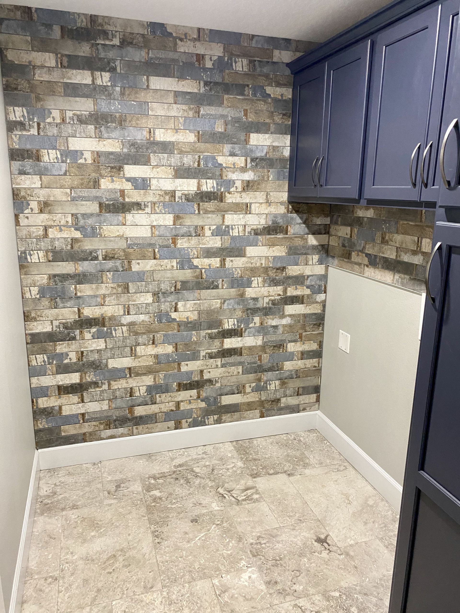 Empty kitchen corner with stone accent wall, navy cabinets, and unfinished floor area