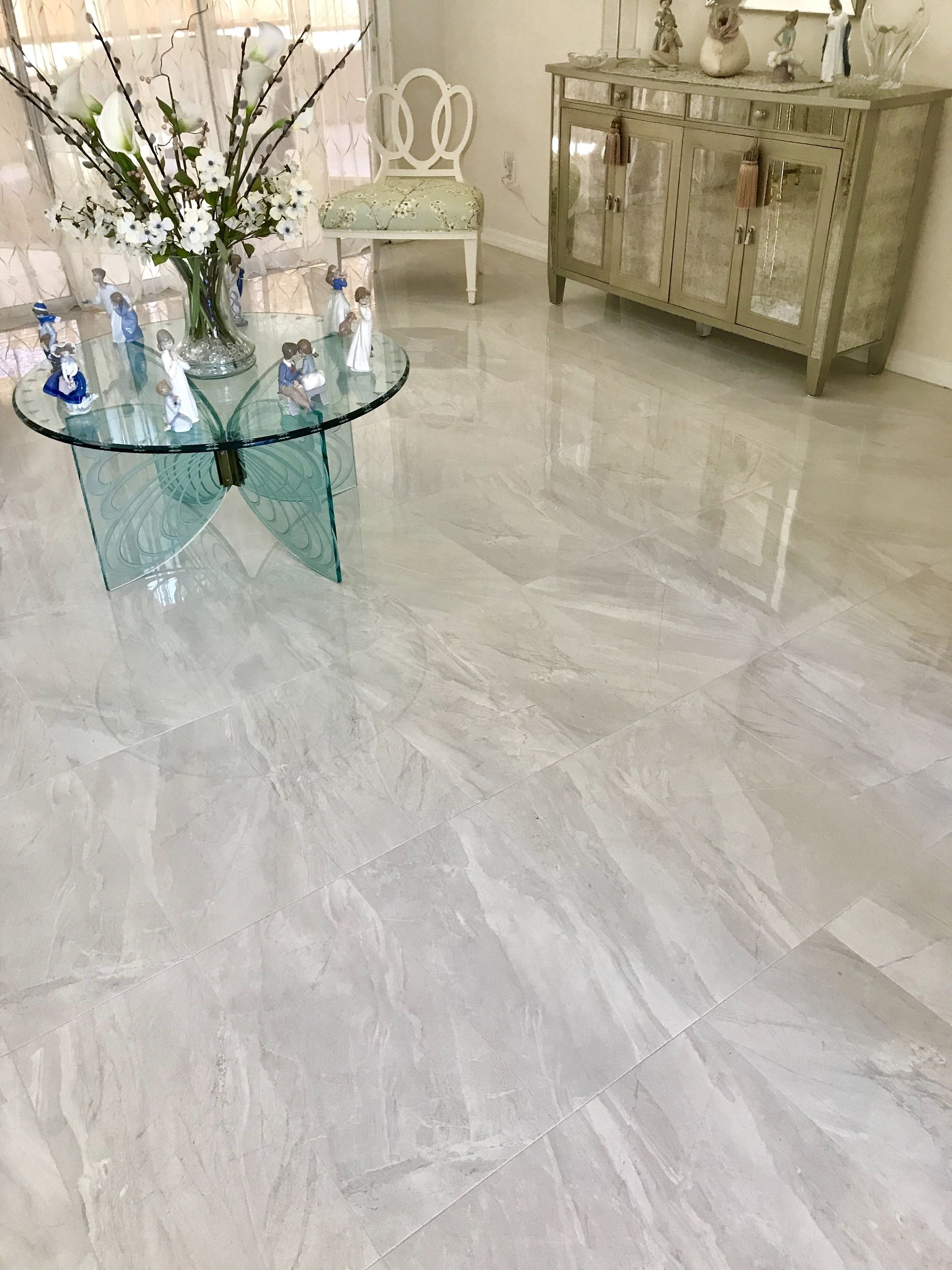 Elegant living room with glass coffee table, white chairs, floral arrangement, and marble floor