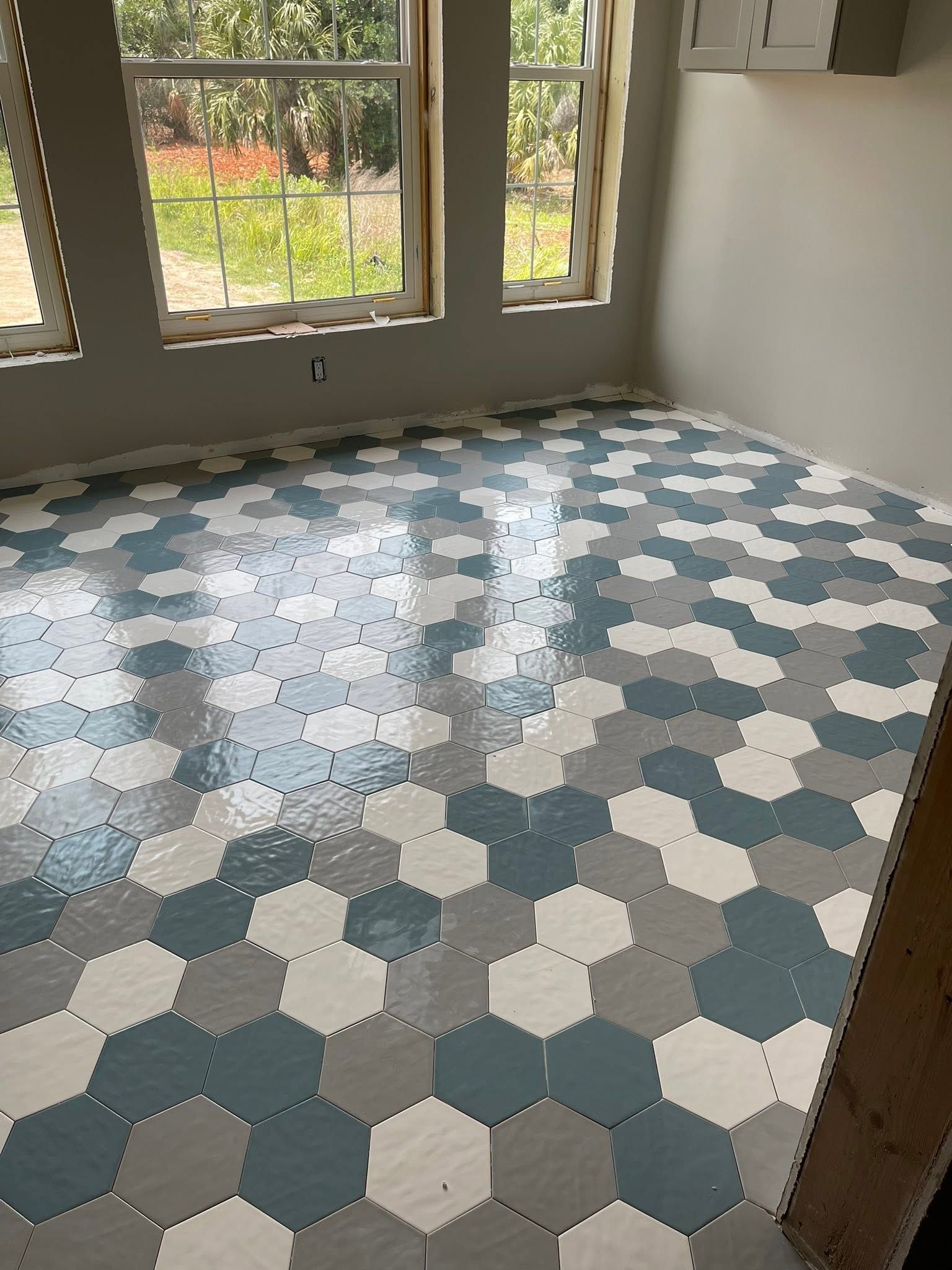 Empty room with blue, gray, and white hexagon-tiled floor and large windows overlooking greenery