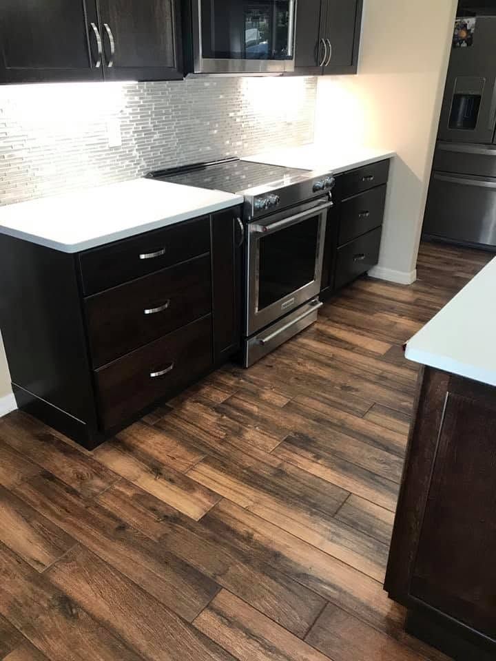 Modern kitchen with dark cabinets, stainless oven, white countertops, and wood-look flooring
