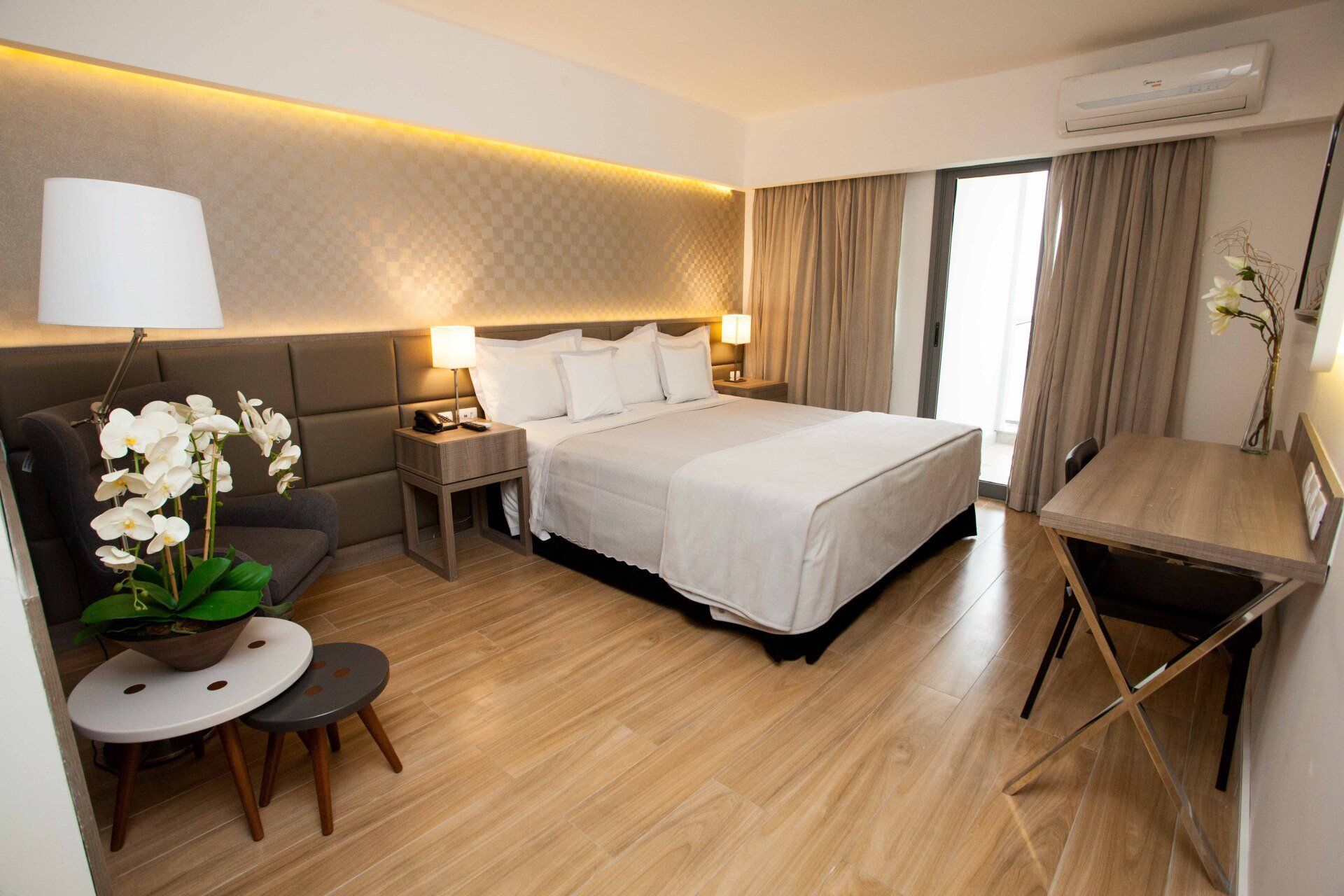 Um quarto de hotel com uma cama grande, escrivaninha, cadeira e luminária.