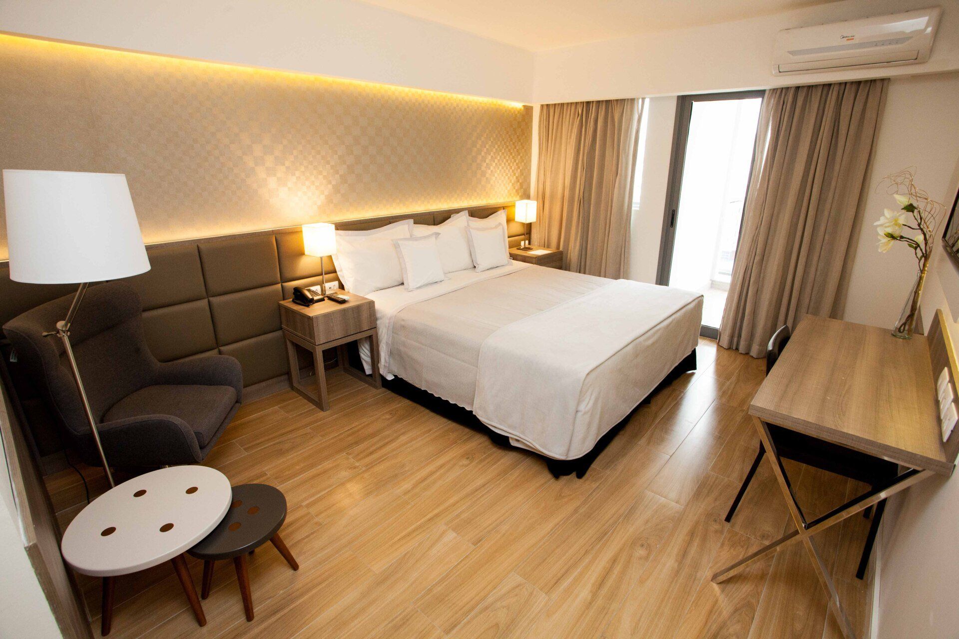 Um quarto de hotel com uma cama king size, escrivaninha, cadeira e luminária.