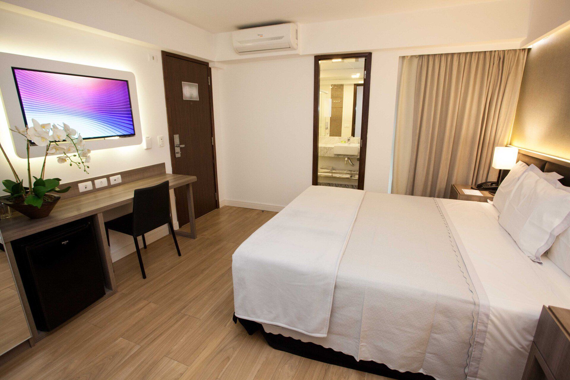 Um quarto de hotel com uma cama, escrivaninha, cadeira e televisão.