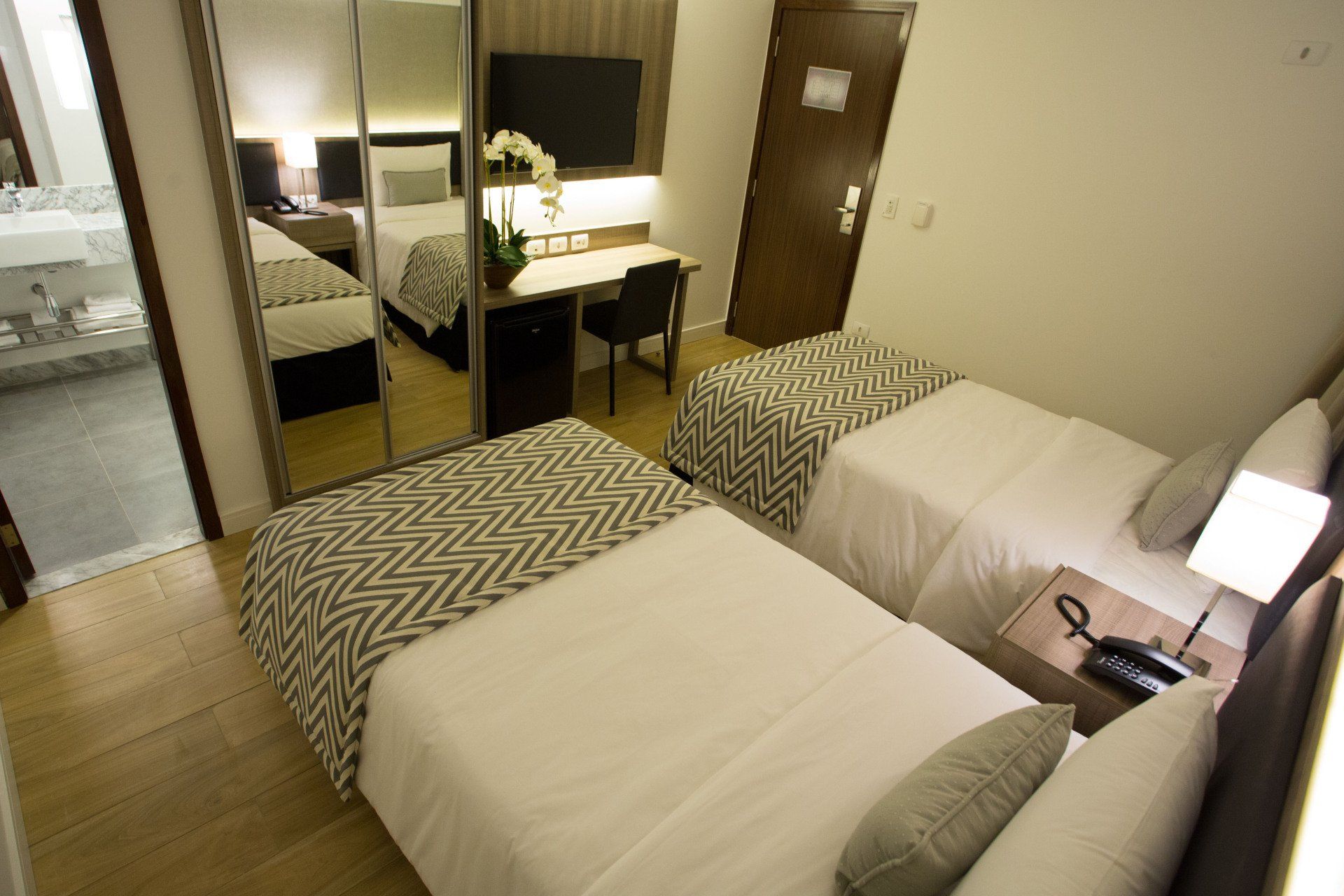 Um quarto de hotel com duas camas, uma escrivaninha e uma televisão.
