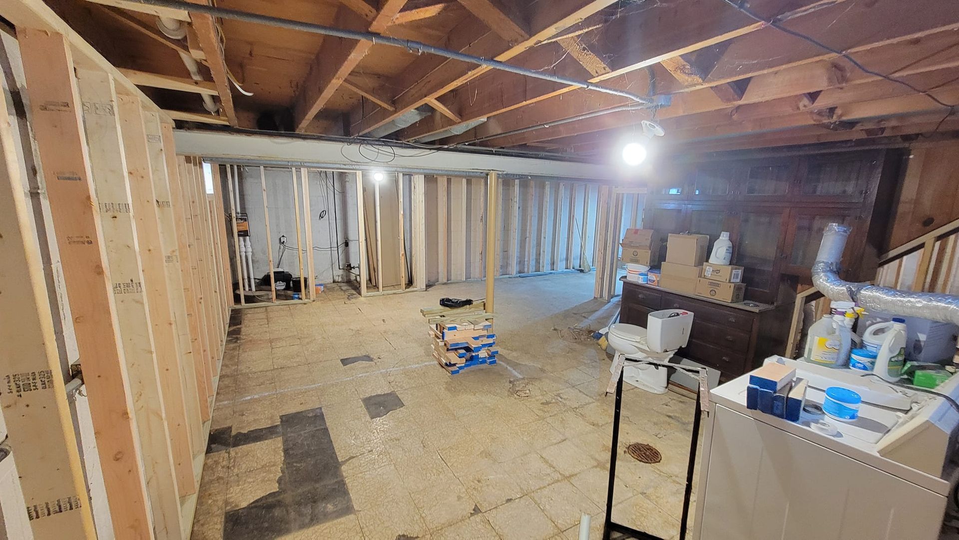 Unfinished basement interior with wood-framed walls, exposed ceiling joists, and various boxes and supplies on the floor.