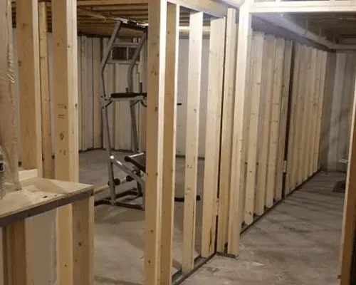 A partially constructed basement room with wood wall framing and an exercise tower standing on a concrete floor.