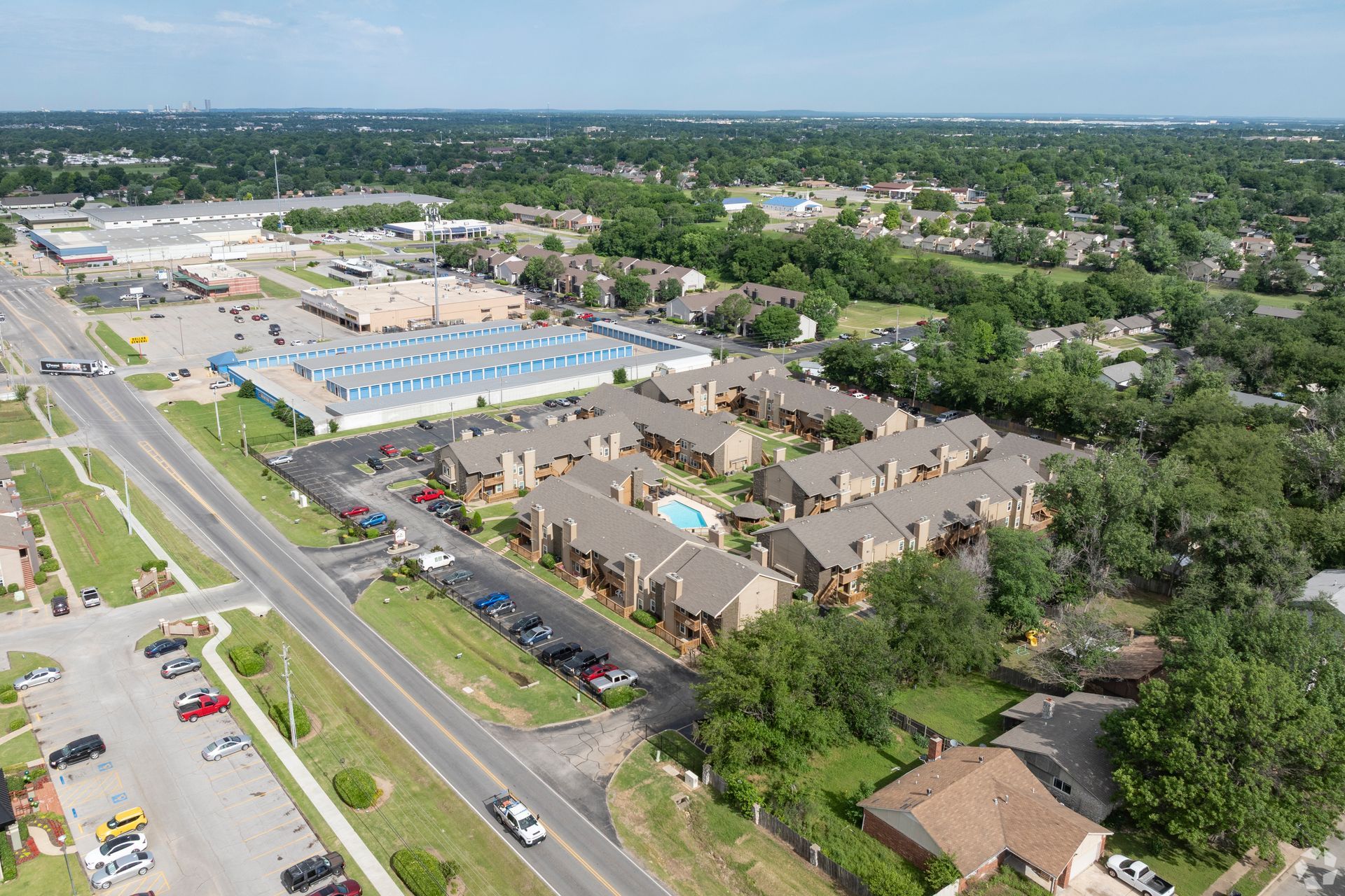 Aerial view of an apartment complex, parking lots, and a busy road on a sunny day.