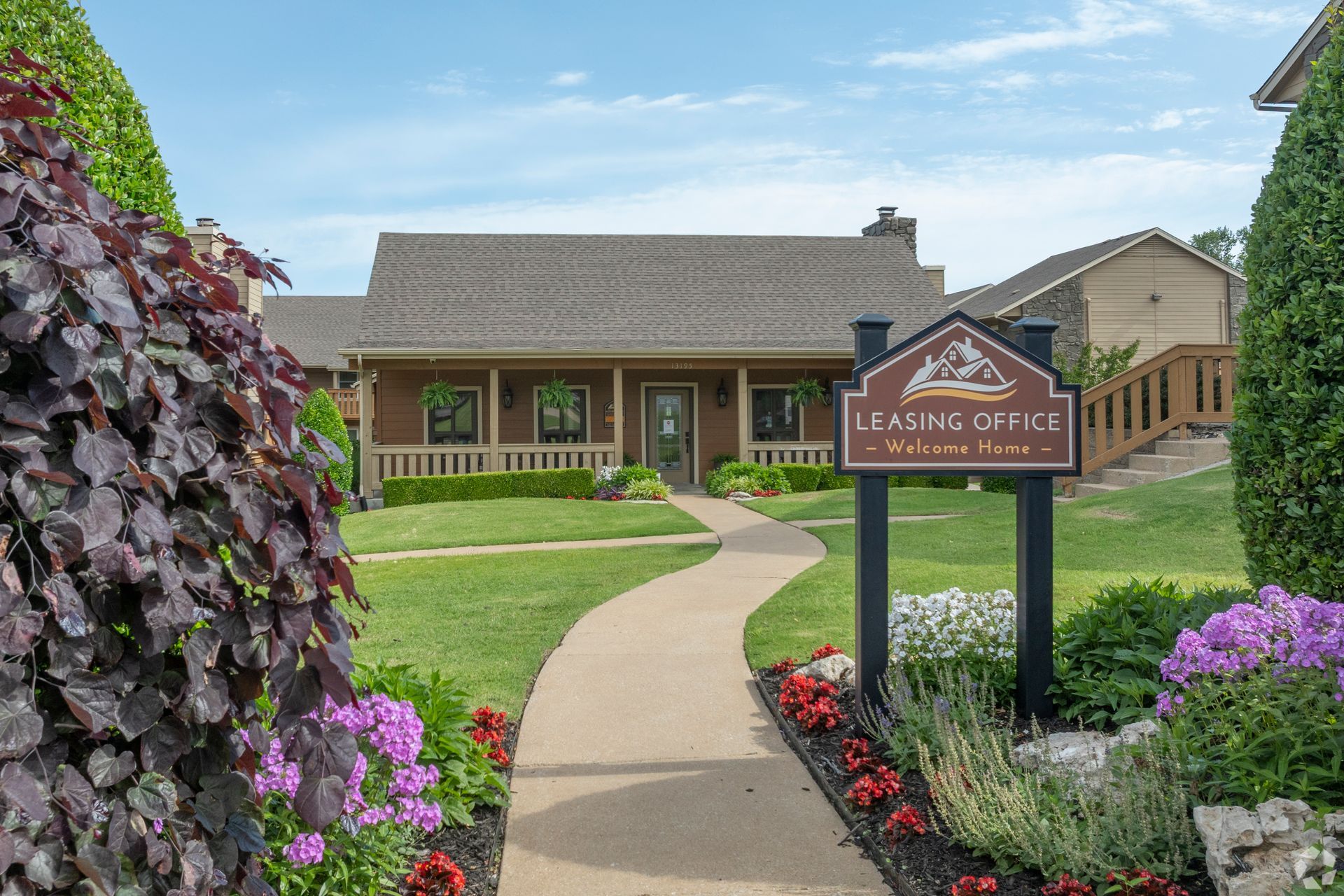 Lush landscaped garden path leading to a leasing office building with a sign in front