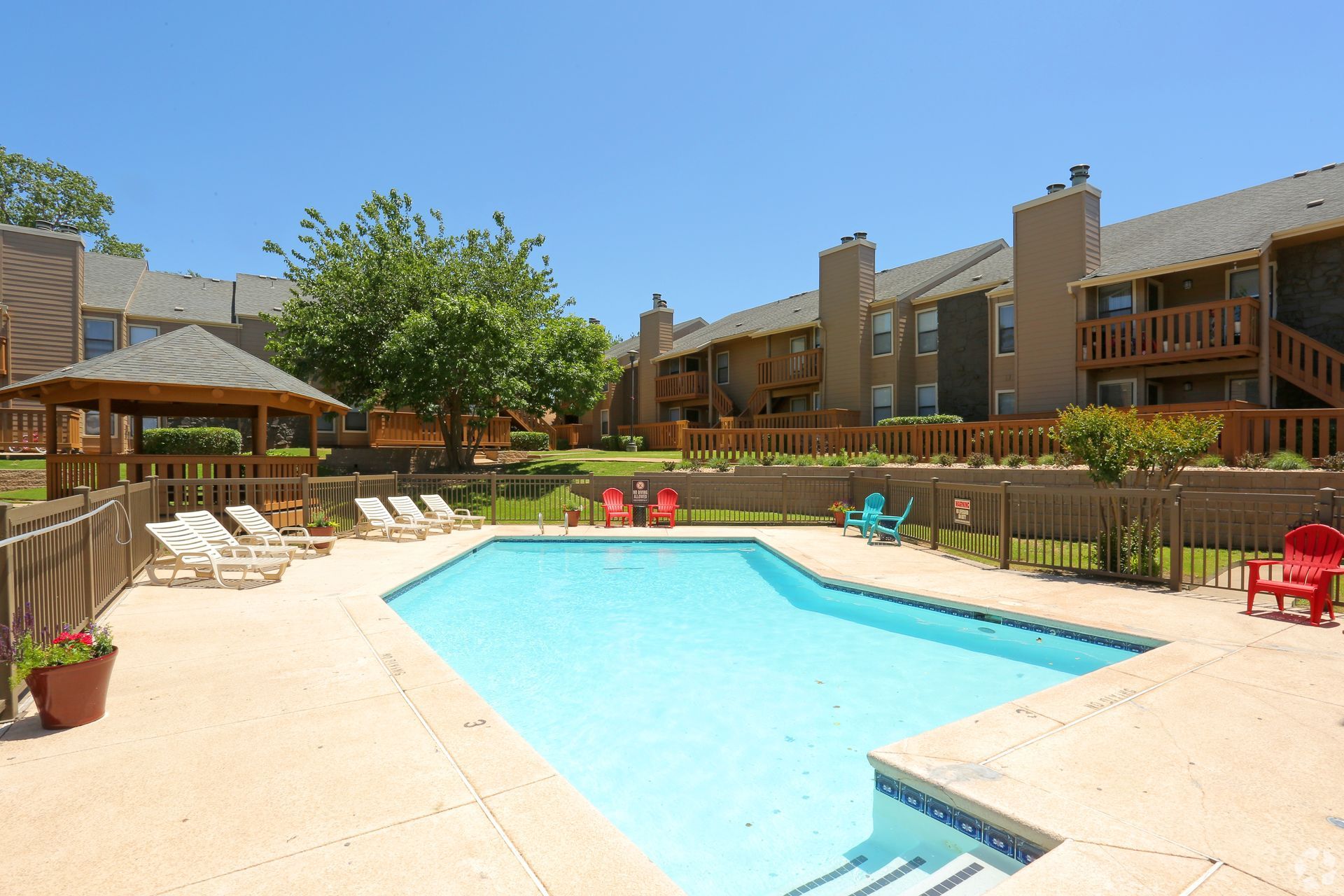Apartment pool courtyard with turquoise pool, lounge chairs, and brick buildings under a blue sky