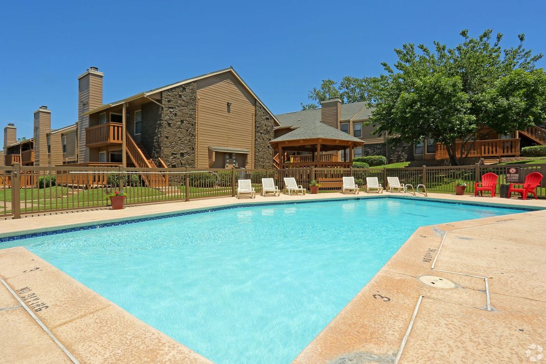 Outdoor swimming pool beside a rustic lodge with lounge chairs and picnic tables under a blue sky
