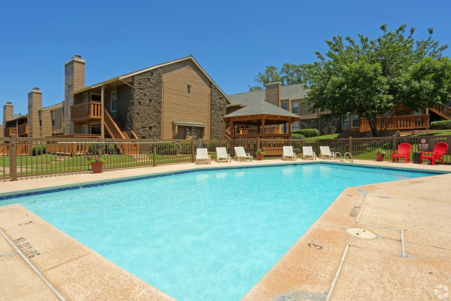 Outdoor swimming pool beside a rustic lodge with lounge chairs and picnic tables under a blue sky