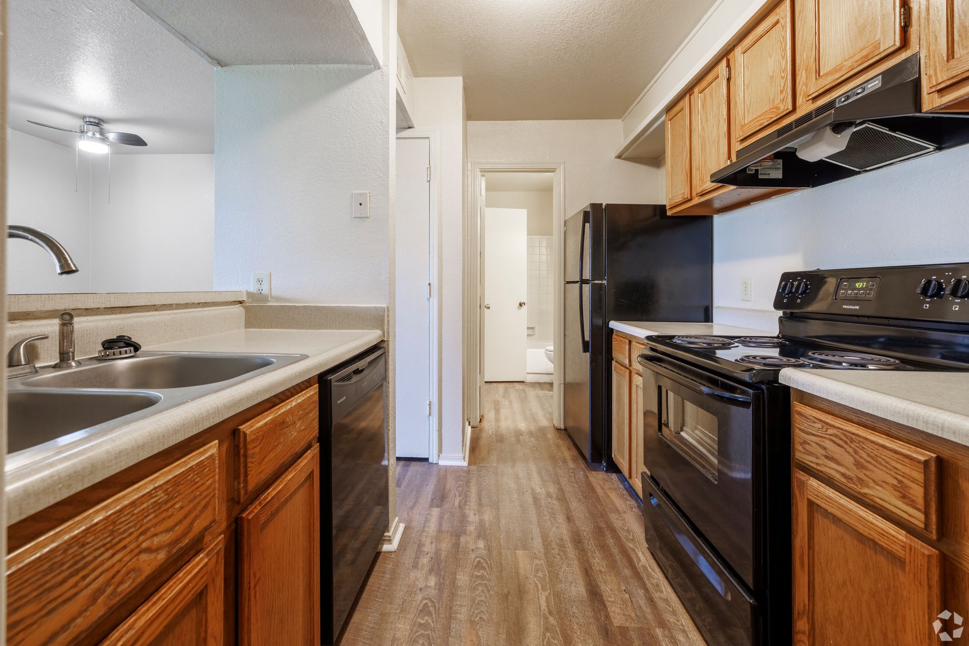 Narrow galley kitchen with wood cabinets, black appliances, and wood-look flooring.