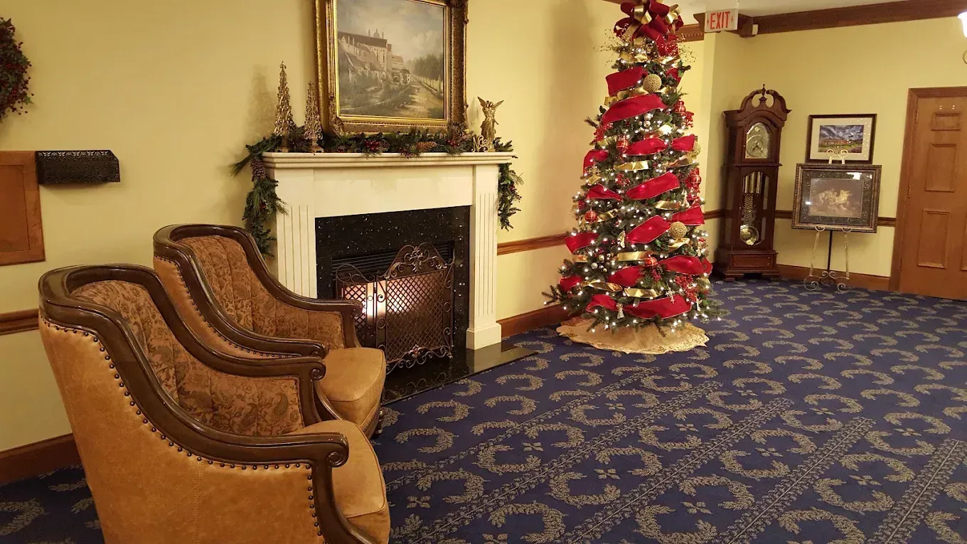 Christmas-decorated room with fireplace, two armchairs, and a lit tree on blue carpet