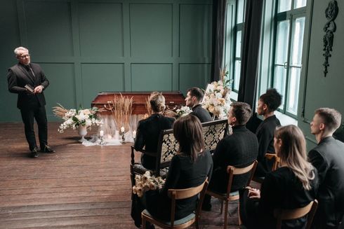 Speaker addressing seated audience in a softly lit room with floral arrangements and chairs.