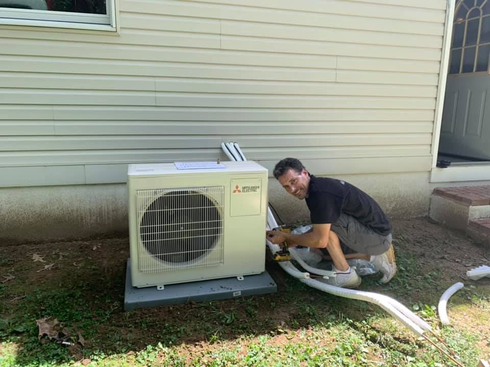 Man installing a Mitsubishi heat pump unit outside a house. He smiles while working.