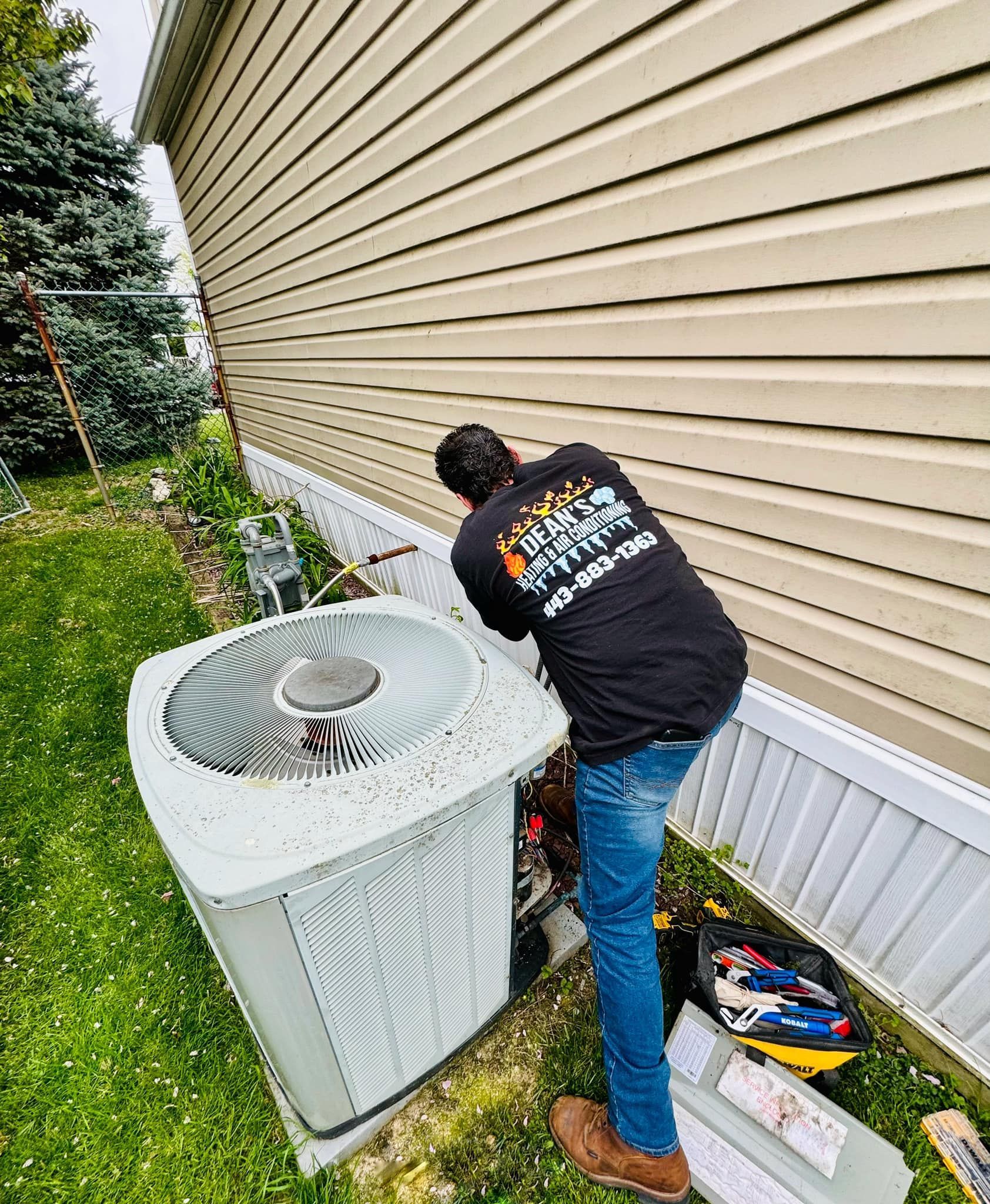 HVAC technician working on an air conditioning unit outside a building with tan siding.