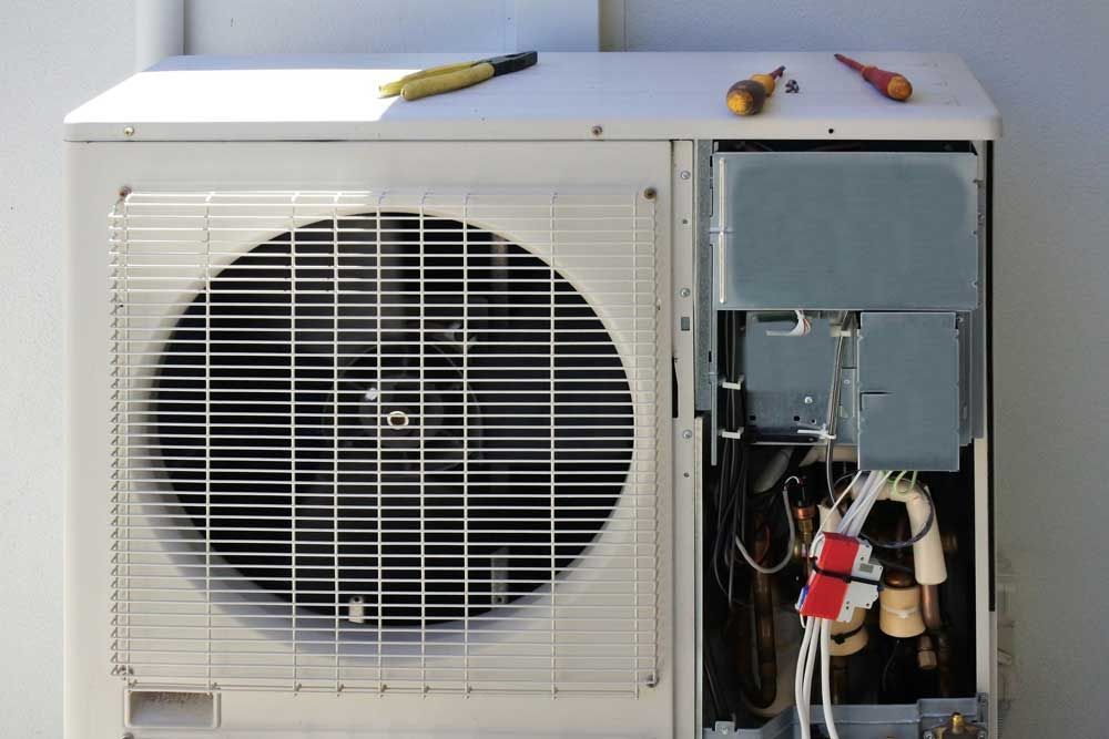 An air conditioner is being repaired with tools on top of it.