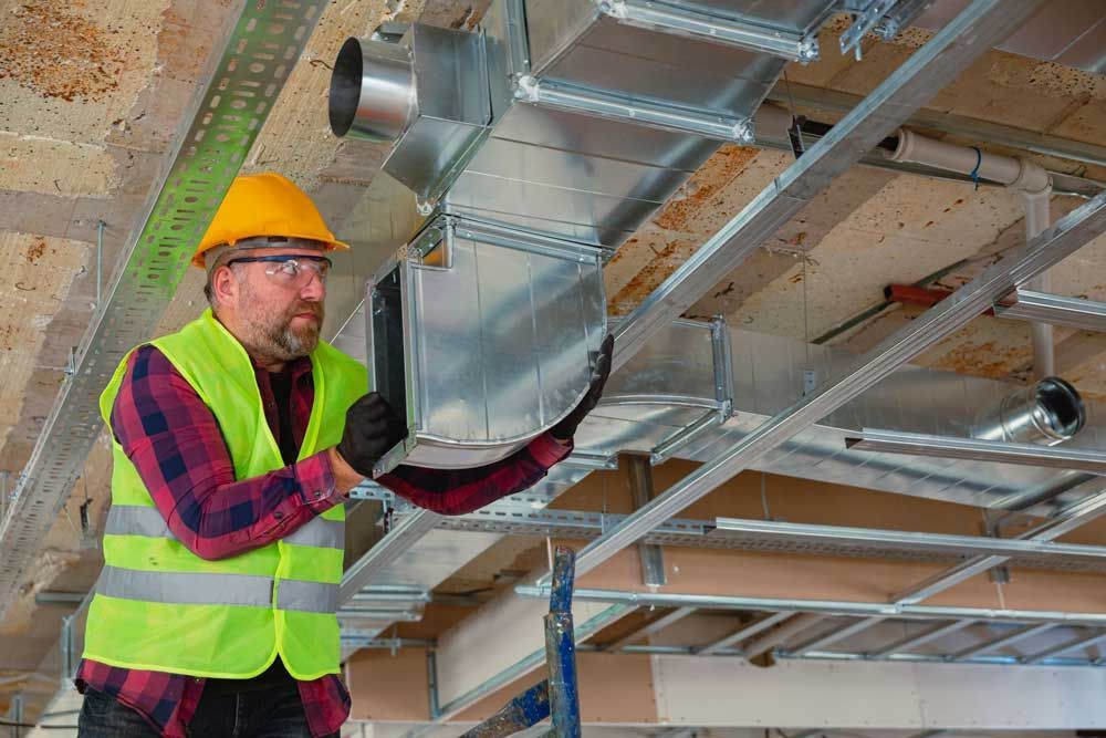 A man is working on a ventilation system in a building under construction.