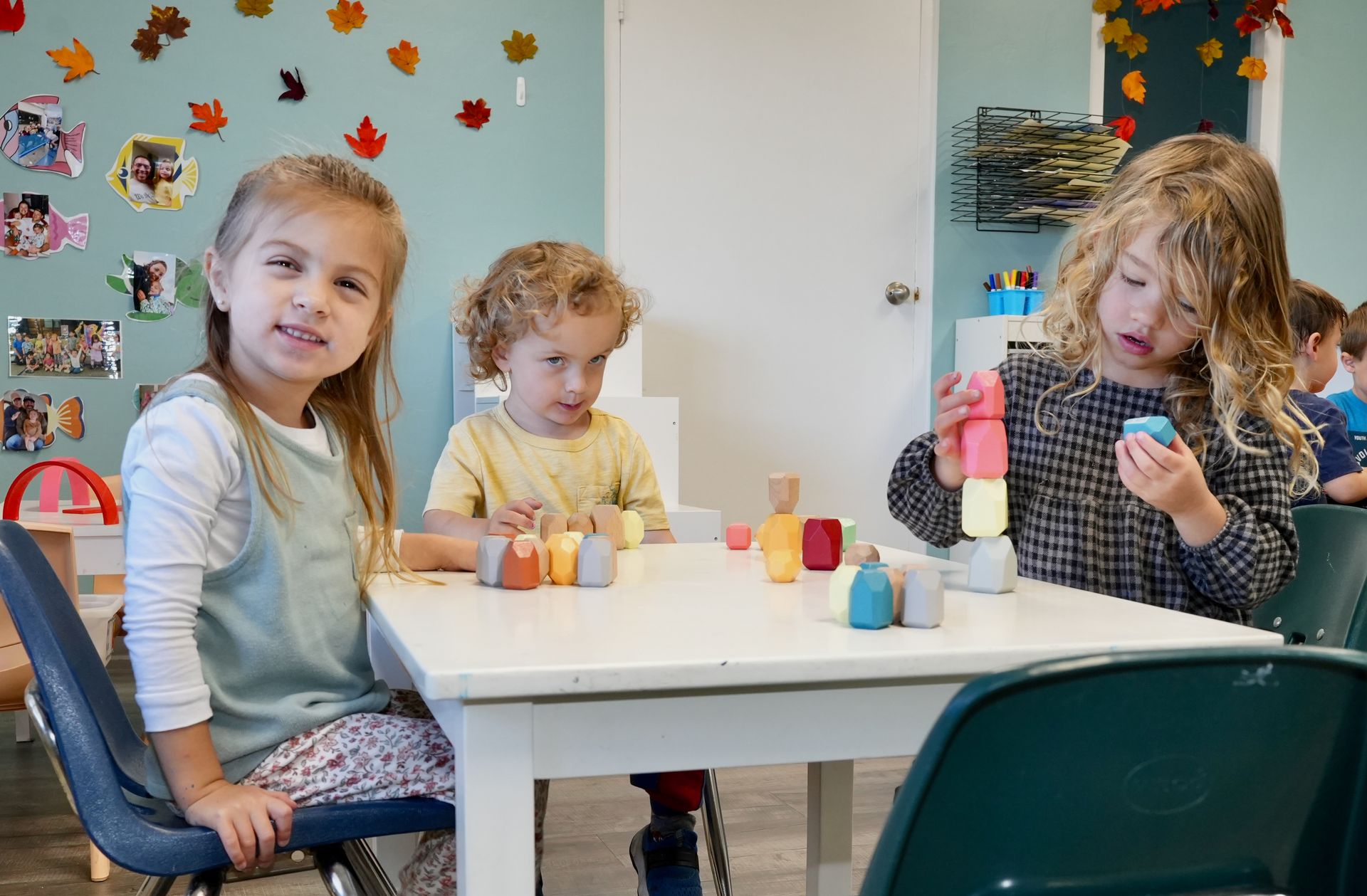 Children painting at a table in a classroom, with colorful art supplies and wall decorations