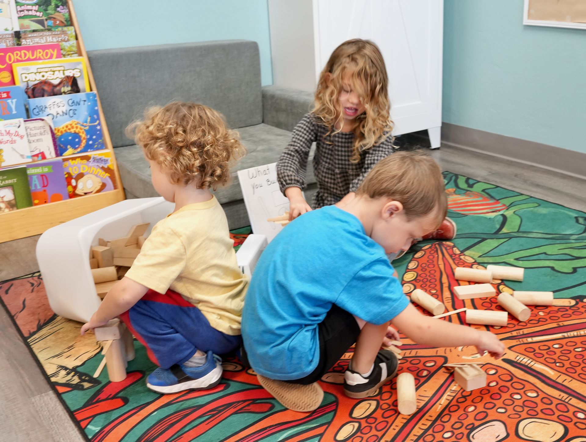 Children playing with wooden blocks on a colorful rug in a classroom corner